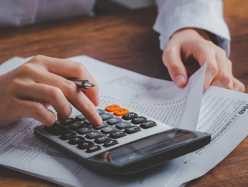Hand using calculator while working on tax documents
